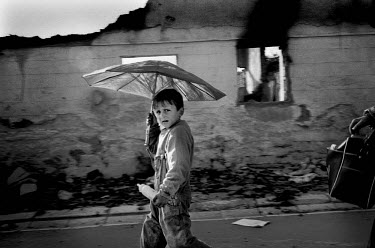 An Albanian boy, with an umbrella to protect himself from the heat, walks through the ruins of Mitrovice.