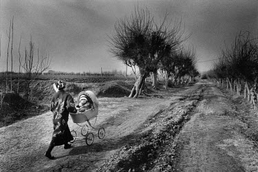 A mother walking with her baby in a pram through the fields of the Ferghana valley.