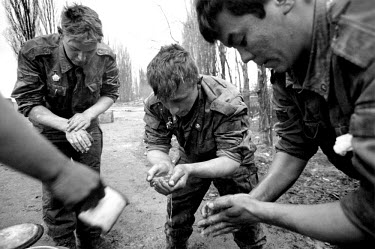 Russian soldiers in Chechnya. Four of them attempt to wash from the same jug of scarce water in the morning after their watch at a battle post.