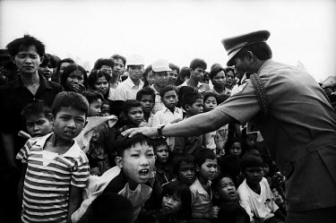 A crowd of refugees recently returned from Thailand are held back by a policeman as they wait to greet King Norodom Sihanouk. A helicopter was returning him from exile to become head of state again.