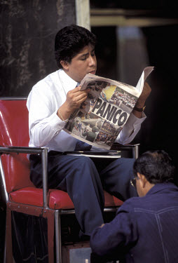 A businessman reads his newspaper whilst his shoes are polished.