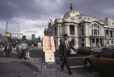 A businessman on his way to work passes a newstand for 'El Economista' outside the Palacio de Bellas Artes.