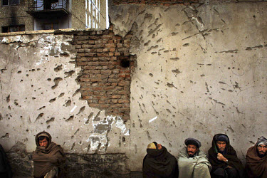 Men sit next to a wall which suffered a direct hit from a rocket.