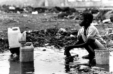 Kid washing clothes in a muddy pool in the slums.