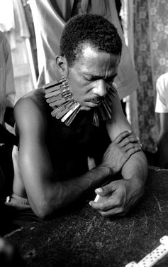 Man playing dominoes in the Cite Soleil district. Every time he loses he has to put another peg on his face.