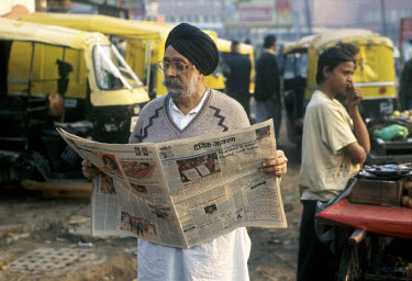 Sikh man reading Hindi newspaper, in the early morning outside New Delhi railway station.