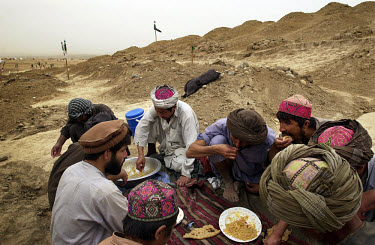 Cemetery on the edge of a refugee camp. The gravediggers take a break to eat lunch. There were at least 100 newly-dug graves.