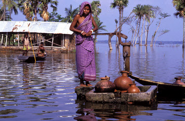 Woman collecting water from a well stranded by rising flood waters, Beel Dakatia.