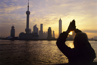 Old man performing morning exercises on the Bund, facing towards the rising sun and the new skyscrapers of Pudong District, including the 457m Oriental Pearl TV Tower.