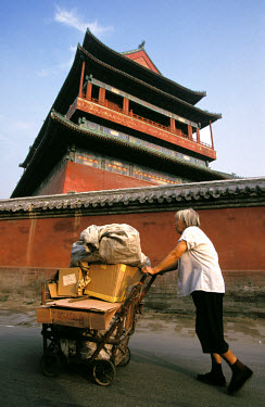 Old woman pushing cart of collected cardboard to sell for recycling, passing behind the Gulou (Drum Tower).