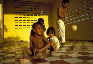 Double amputee landmine victim playing with a football at a rehabilitation centre, passing children of other victims.