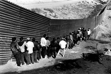 Migrants queuing beside the fence which marks the American-Mexican border. Since a clampdown by the border patrols, many people have been left in limbo on the Mexican side, unable to carry on or to re...