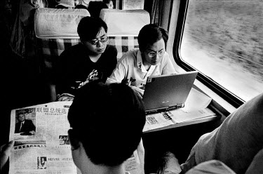 Commuters on a city train reading the newspaper and working on a laptop computer.