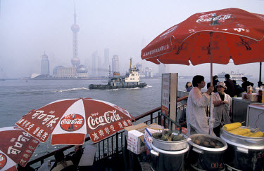 Coca-cola umbrellas stand over food stalls on the Bund, with the Pudong new financial district and the Orient TV tower on the far side of the Huangpu River.