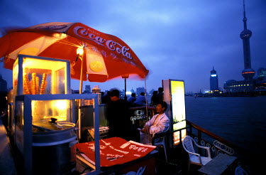 An ice cream stall, decorated with Coca-Cola advertisements, during twilight on the Bund.