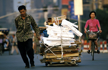 Poor man pulling cart loaded with polystyrene that he has collected to sell for a small sum to a recycling business.