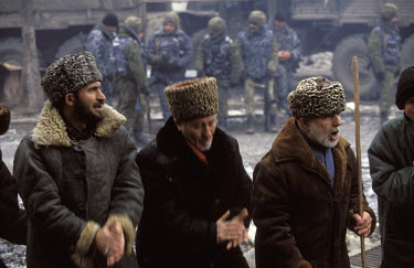 Chechen men dance and sing religious songs in protest at the Russian occupation of Chechnya, while Russian special forces soldiers stand a few metres behind them.