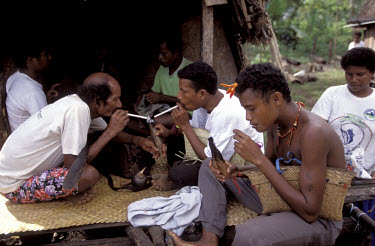 Youths share cigarettes in their bachelor house. Kiriwina.