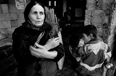 A mother warms herself from the cold while her two sons cuddle together outside their home, an abandoned rural train station. Refugees from the conflict in Nagorno Karabakh, they took shelter here six...