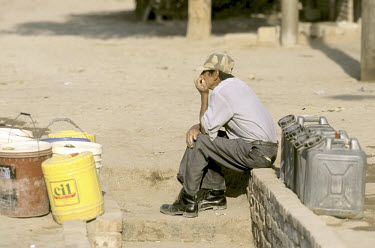 A man waits beside a water pump. Water is usually only available for 30 minutes per day.