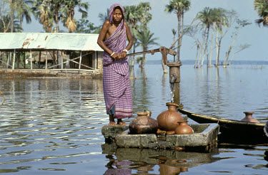 Woman collecting water from a tube well stranded by rising flood waters on Beel Dakatia.