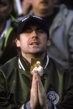 A Celtic supporter prays during a match against Rangers, with a photograph of Pope John Paul II providing spiritual guidance. The 'Old Firm' rivalry between Celtic and Rangers is renowned as the world...