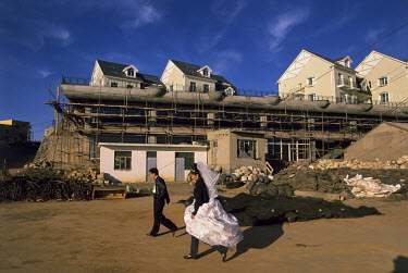 Bride and groom after a session taking wedding photographs on the sea front with a hired Western-style dress, passing new villas under construction in the Dalian development zone, 50 kilometres from t...