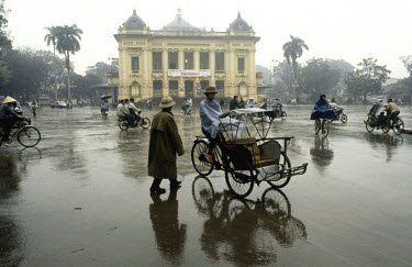Cyclo in typical winter rain passing the Municipal Theatre, the former French colonial-era Opera House.