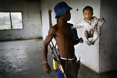 War child. A government militiaman proudly shows off his son. Several dozen fighters and their families are currently living in the former head offices of the national bank of Liberia in downtown Monr...