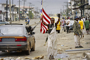 LURD rebels on Bushrod island celebrate a ceasefire. A LURD fighter holds the Liberian flag aloft as other fighters drive past in a looted vehicle. Bushrod Island is economically important, as the Fre...