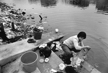 Woman washing clothes in the Lianjiang River beside the computer waste dump. What was once a poor farming region has become a promised land thanks to the e-waste business. But Guiyu is no glittering s...