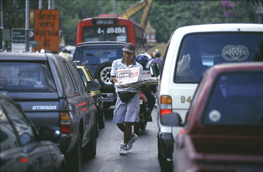 Man selling newspapers on highway to drivers stuck in morning rushhour traffic jam.