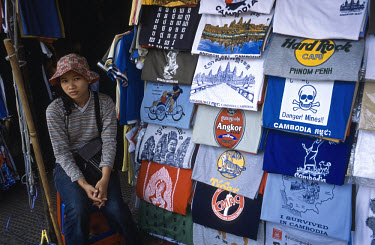 Central Market (Psar Themei). Young woman with T-shirts for sale, including images of Angkor Wat and 'Danger! Mines!'