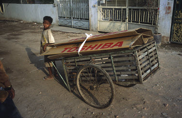 Child with cart full of cardboard collected to be re-sold for recycling, the upper piece bearing Japanese company Toshiba's name.