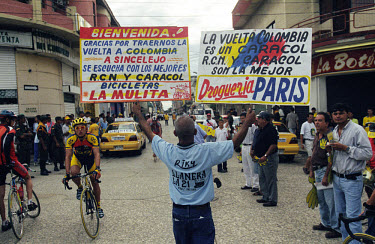 A man hold up placards welcoming the Vuelta a Colombia to Sincelejo and advertising local stores. The 53rd Vuelta a Colombia took place against a backdrop of civil war and violence. The bicycle race i...