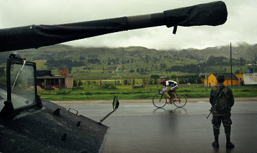 Competitor in the Vuelta de Colombia passing a soldier and a tank guarding the route of the Tour. The 53rd Vuelta a Colombia took place against a backdrop of civil war and violence. The bicycle race i...