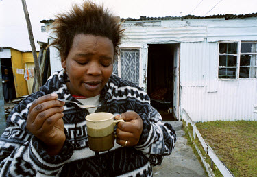 A woman enjoys a cup of coffee outside her township home on a chilly winter morning.