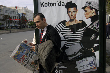 Man reading newspaper, smoking, next to bus stop advertising a Turkish bank's Visa credit card.