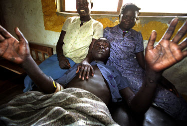 Sleeping Sickness ward in the village hospital. A young man is calmed by his sister. He is in stage two of the disease where the parasites in his blood begin to affect his brain. At times he needs re...