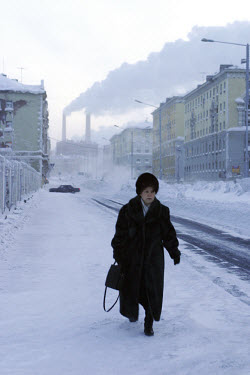 A woman walks down a snowy street in temperatures of minus 30 degrees celsius. In the distance is a power plant. Residents of this resource-rich city above the Arctic Circle in Siberia battle long pol...
