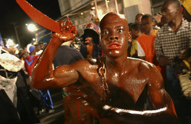 A man covered in fake blood to illustrate the terror of slavery marches in a carnival procession.