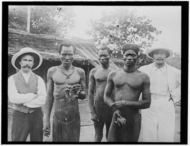Two British missionaries with Congolese men holding the severed hands of two men (Lingomo and Bolenge) from their village, murdered by rubber sentries from the ABIR (Anglo-Belgian India Rubber company...