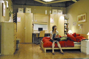 A woman sits down on a bed and yawns in the bedroom department of Ikea.