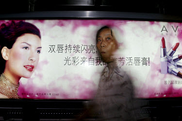 An old woman passes a poster advertising lipstick.