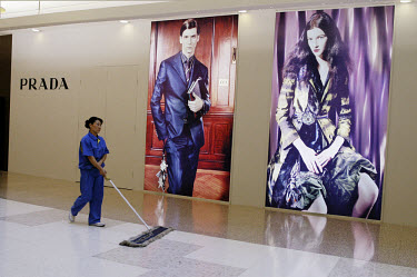 Cleaner walks past Prada store posters.