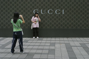Girls pose for photographs in front of a Gucci store.