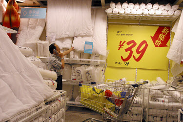 A man looks at duvets in Ikea while making a call on his mobile phone.