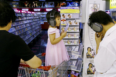 A young girl listens to music in the CD section of a supermarket.
