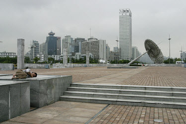 A man sleeping in the barren modern cityscape.