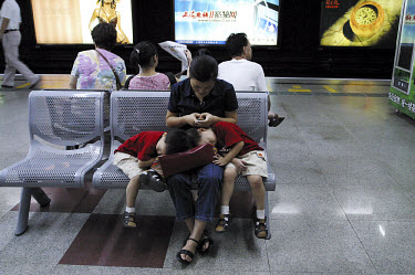 A woman sends a text message (SMS) from her mobile phone while waiting for a train in the metro with her twin sons asleep on her lap.